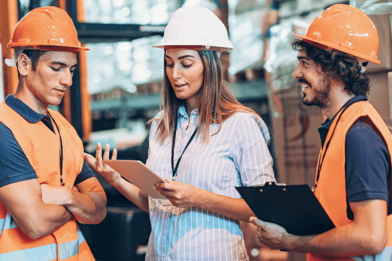 Three warehouse workers whearing hardhats and bright orange reflective safety vest