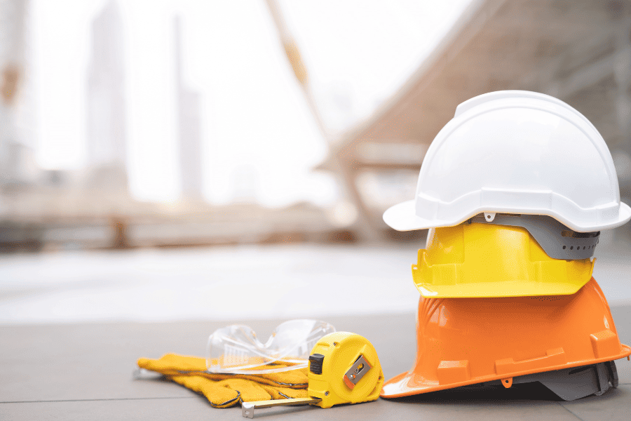 Three hardhats, next to safety glasses, measuring tape and wrok gloves